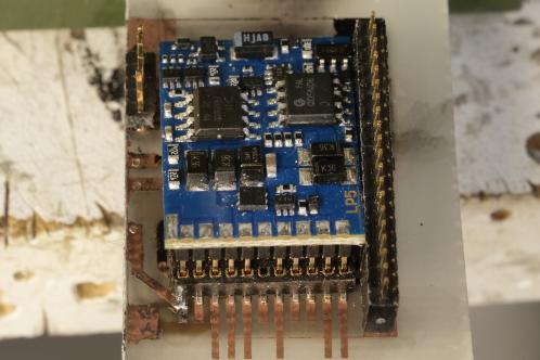 Een klein blauw electronicaprintje vol met SMD-onderdelen (een ESU Lokpilot V5 decoder) en meerdere 1,27 millimeter headers op een ander electronicaprintje