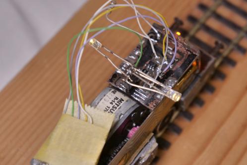 Een modeltrein zonder kap met zicht op een electronicaprint met aangesoldeerde draden die met plakband tijdelijk gefixeerd zijn, en 3 LEDs snel gesoldeerd aan een 4-polige header