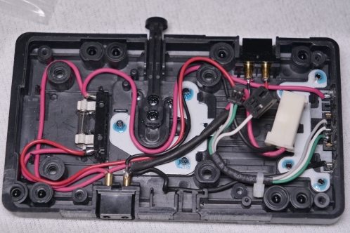 Een zwart plastic plaat met bedrading en metalen onderdelen en twee voedingsaansluitingen, een V-mount accuplaat van IDX