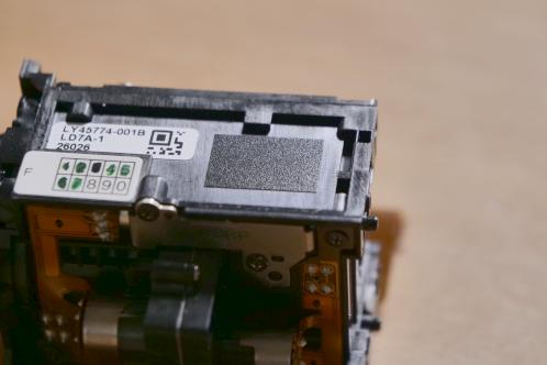 Een stukje matzwart tape op een zwart plastic blok, het optische blok van een JVC-GY-HM100 videocamera