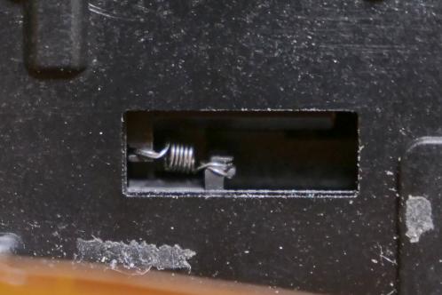 Een zwart plastic blok met twee kleine pallen als onderdeel van de zoom-motor in het optische blok van een JVC-GY-HM100 videocamera, met nieuw gemonteerd anti-backlash veertje