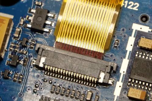 Een goudkleurige flexibele print die in een connector op een blauwe electronicaprint steekt
