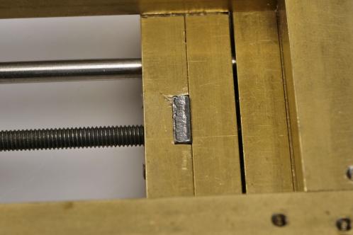 De onderzijde van een zelfbouw-bankschroefje uit messing, met de moer voor het schroefdraad waarmee de bekken gesloten worden zichtbaar opgesloten tussen twee messing helften