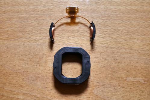 Een zwarte plastic houder met lenzen en flex-print eenheid die over de plastic houder schuift, onderdelen van de optische stabilisatie van een JVC-GY-HM100 videocamera