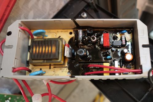 Een grijze kunststof behuizing met elektronicaprint met diverse onderdelen waaronder een hoogspanningstrafo en hoogspanningscondensatoren, in de behuizing gemonteerd met een zwarte hars, de hoogspanningsmodule voor een vliegenlamp