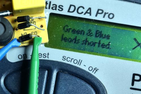 Een elektronicaprint met enkele diodes enkelzijdig losgesoldeerd, met 1 diode aangesloten op een meet-apparaat dat 'groene en blauwe meetdraad kortgesloten' toont