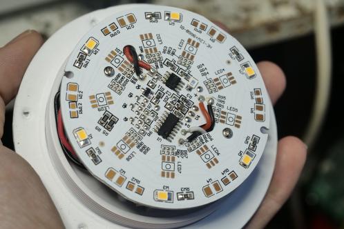 Een witte kuntststof plaat met een witte elektronicaprint met LEDs, weerstanden, enkele condensatoren en enkele IC's, de printplaat van een Le Zen Lux lamp
