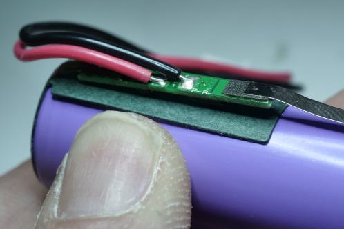 Een lithium cel met kleine groene electronicaprint en aangesoldeerde rode en zwarte draad. Beveiligingsprint van een lithiumcel