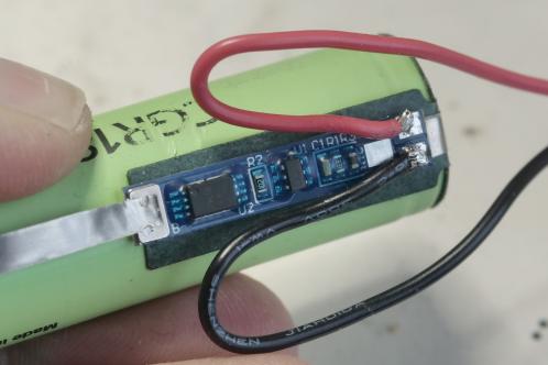 Een groene Panasonic CGR18650 lithium cel met blauwe elektronicaprint met rode en zwarte draad aangesoldeerd, een nieuwe cel met nieuwe beveiligingsprint