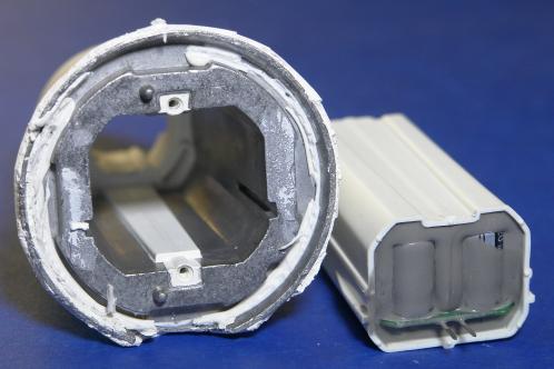 Een trechtervormig aluminium koelblok omgeven met wit kunststof, met rechts ervan de in wit plastic en grijze gietmassa ingegoten voeding van een Osram AC01754 LEDlamp