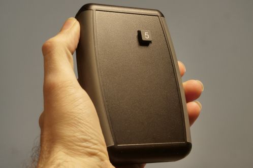 Een zwarte kunststof behuizing in gesloten toestand die volledig in een handpalm past, met een vierkante toets gemerkt met '5' uitstekend aan de voorkant, de nieuwe behuizing voor de afstandsbediening van een Patona DMW-BGGH5RC batterygrip