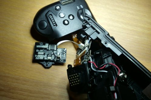 Meerdere zwarte plastic delen van een behuizing geopend, met kleine printplaten met SMD-electronica onderdelen zichtbaar verbonden door een flexcable, de binnenkant van een Patona DWM-BGGH5RC batterygrip