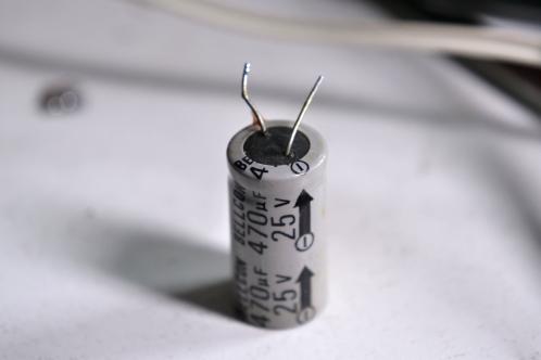 Een cilindrisch grijs onderdeel, een elektrolytische condensator met opdruk in zwarte letters, 470 uF en 25 Volt