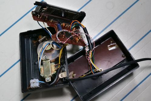Een zwarte kunststof behuizing met daarin meerdere elektronicaprinten met diverse onderdelen, een transformator en een luidspreker, een Good old electric digitale wekker