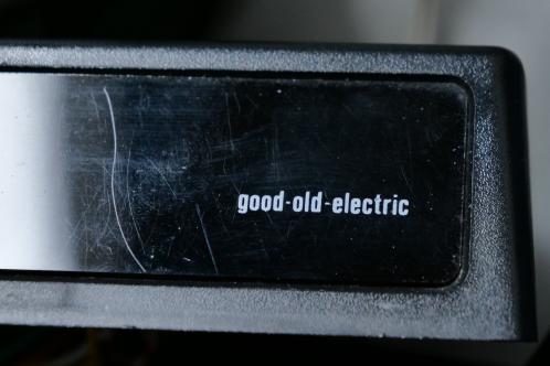 Een zwarte kunststof behuizing met donkergroen transparant venster met daarop een logo met 'good old electric' een digitale wekker
