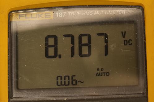 Een grijs LCD-display van een FLuke 187 multimeter geeft 8,787 Volt aan als voedingsspanning voor de schakeling van de Zweedse elektrische kachels