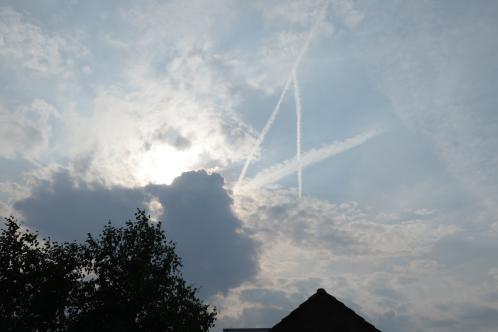 Een boomtop en puntdak van een huis met daarboven een zon die gedeeltelijk door hoge bewolking aan het zicht onttrokken wordt bij nadering van onweer