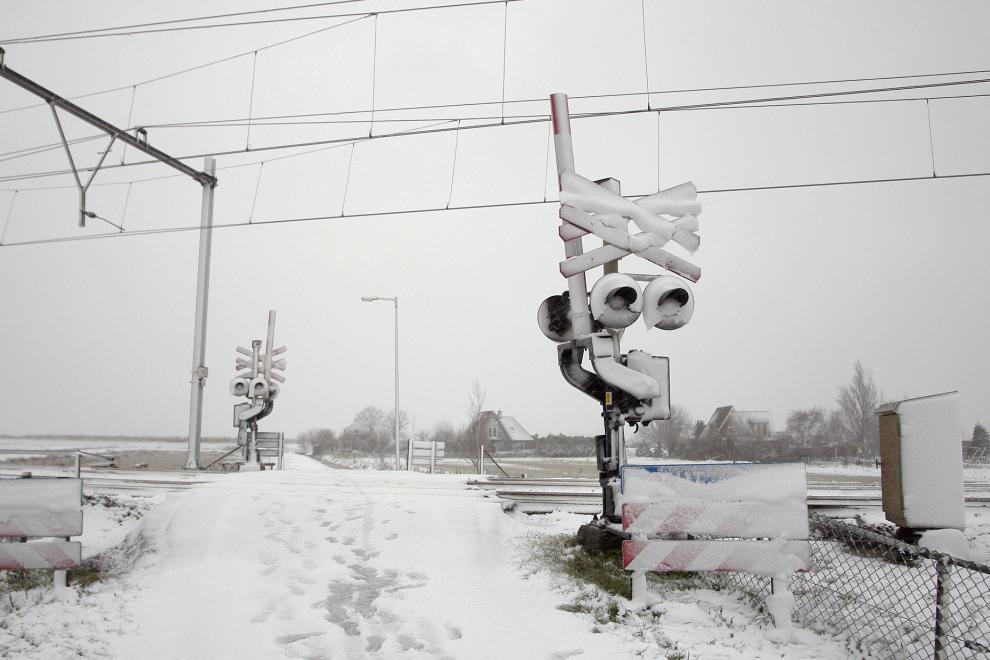 Grijze lucht, volledig witte wegen en omgeving en een spoorwegoverganginstallatie volledig ondergesneeuwd door sneeuwjacht. Overweg Wormerpad in Noord-Holland op 10 december 2017